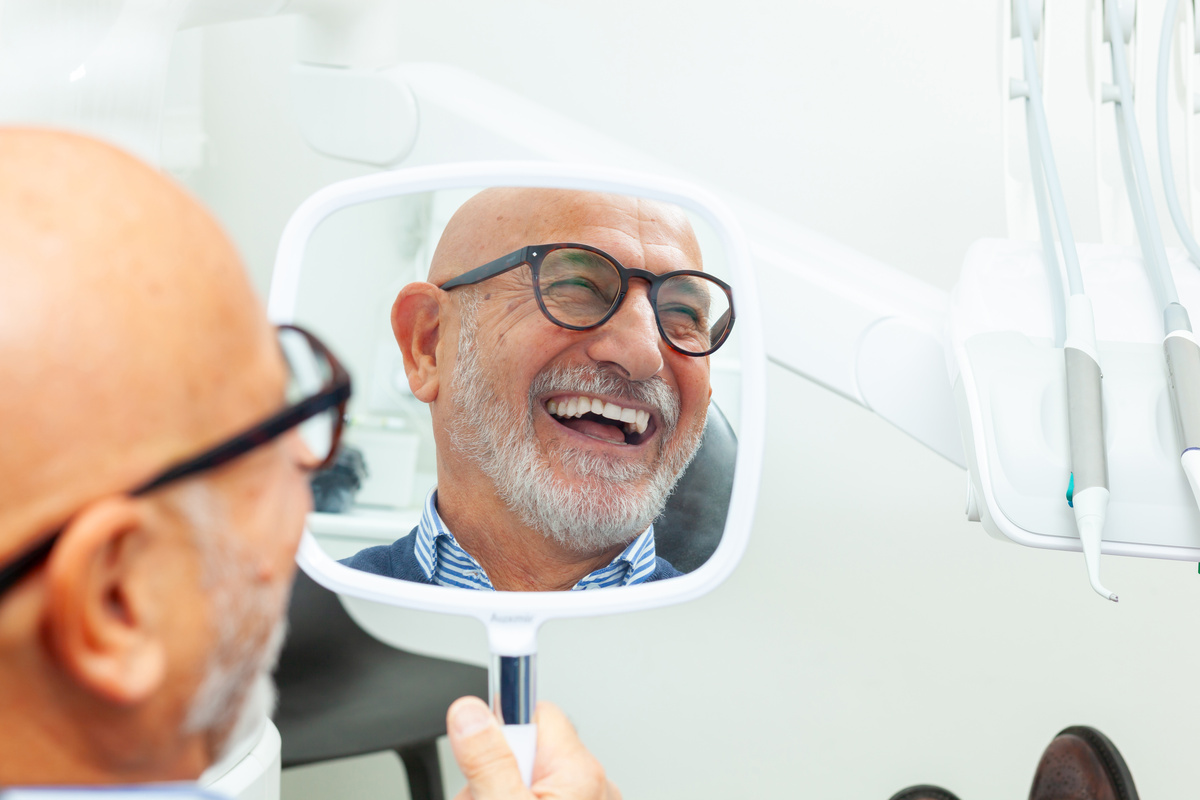 Senior man admiring his new smile in dental clinic mirror