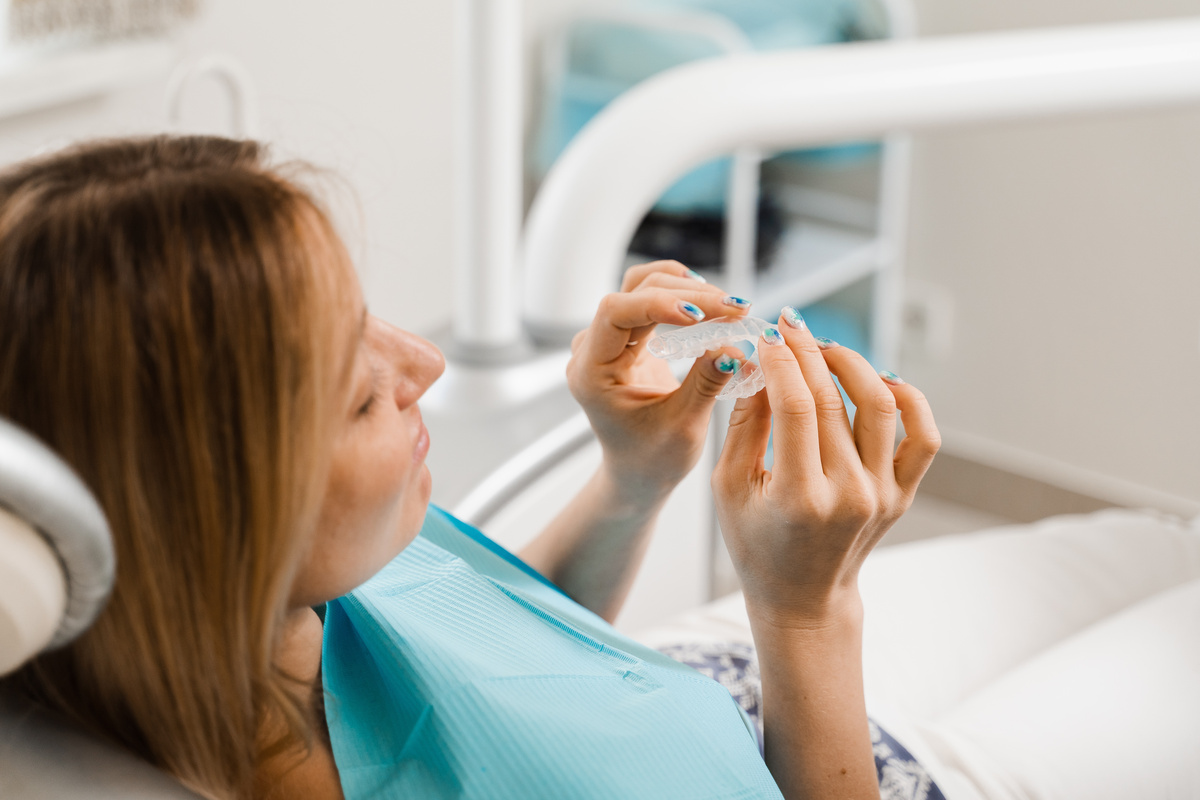Clear aligner for bite correction and shape of teeth. Orthodontist shows transparent removable retainer for patient woman in dentistry.